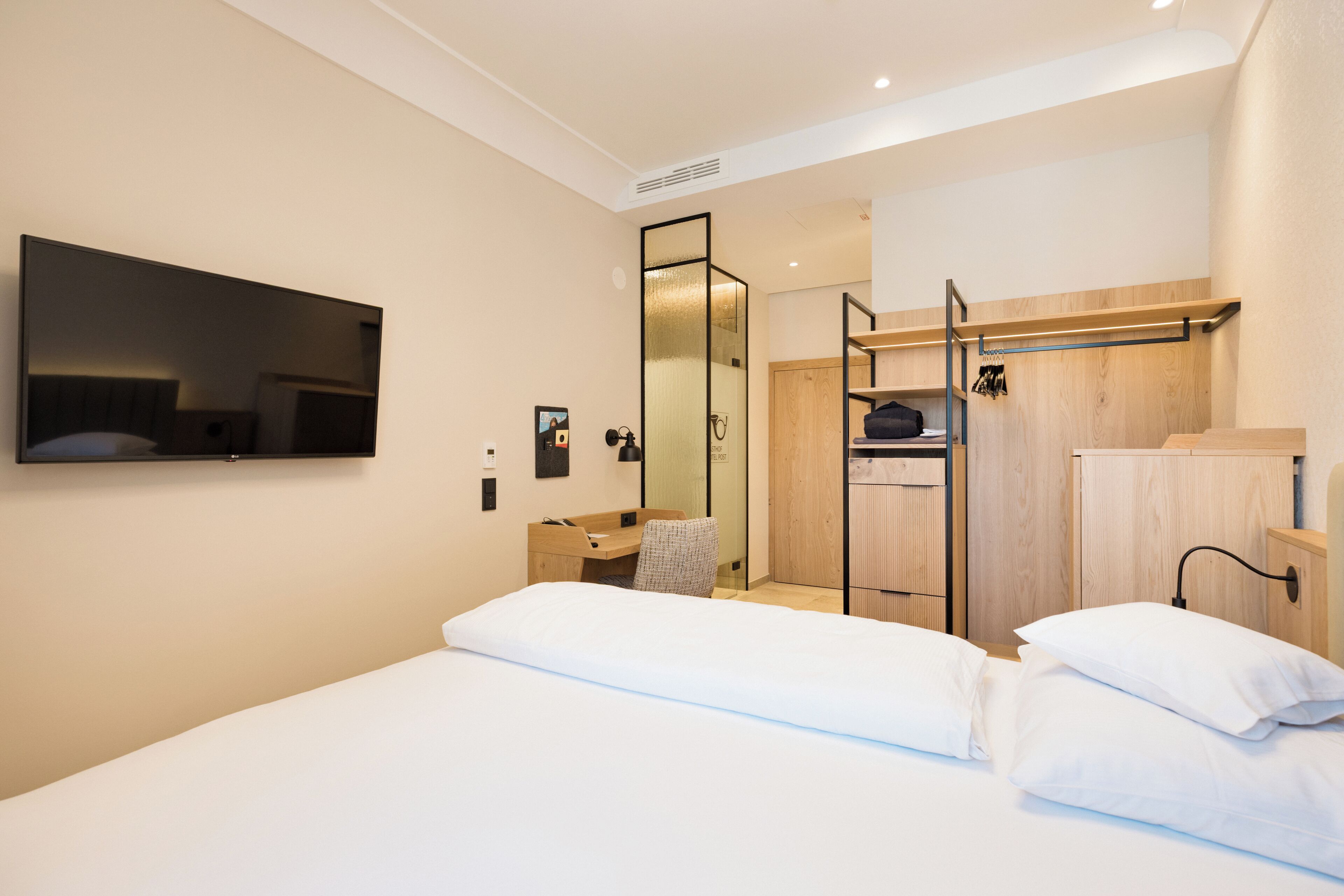 A modern hotel room with a bed, a desk, a mirror, and a wardrobe.