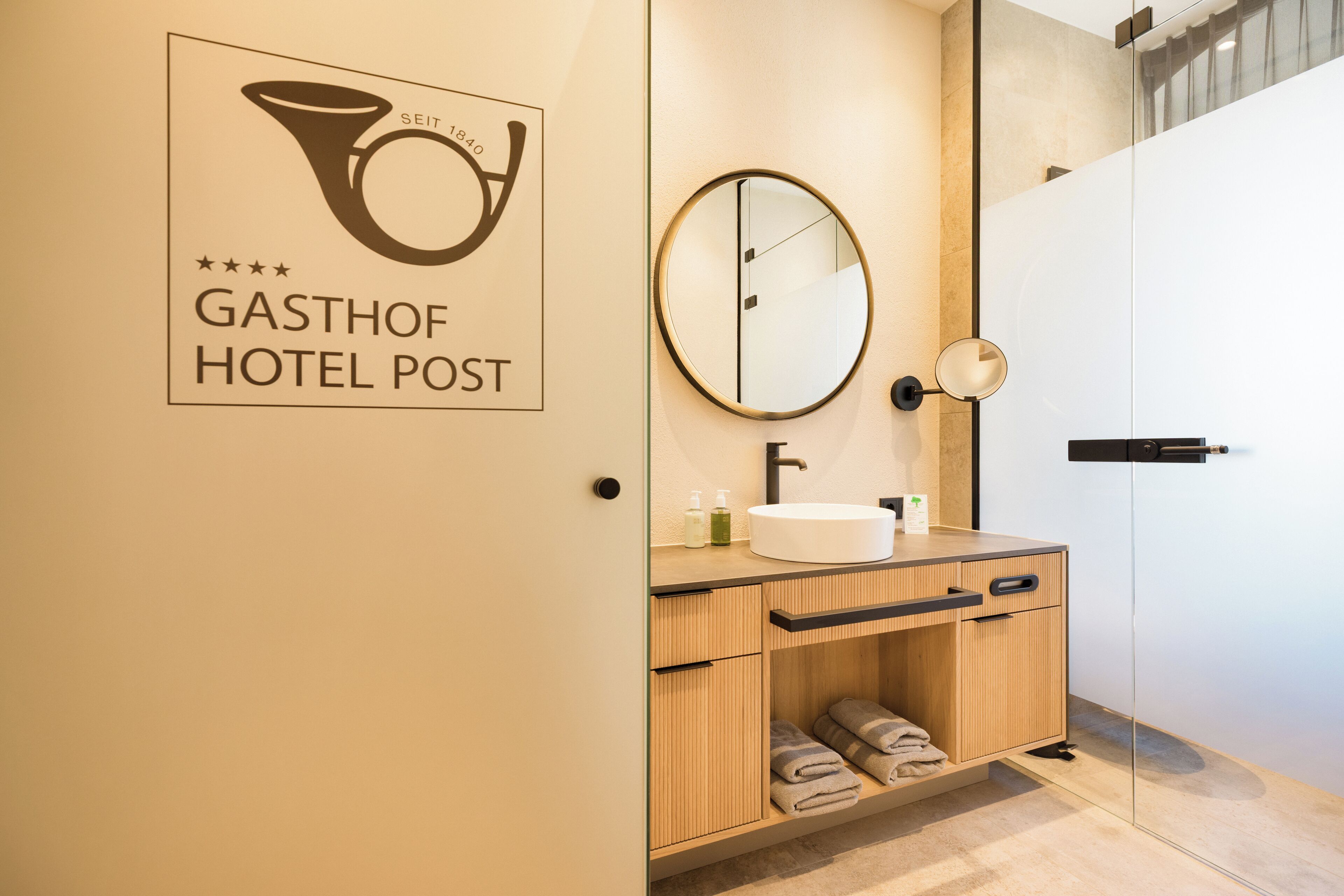 Een moderne badkamer met een houten wastafelmeubel, een ronde spiegel en een wastafel.