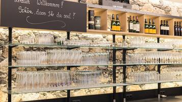 A bar area with a stone wall background, shelves with wine bottles, and a sign with a greeting in German.