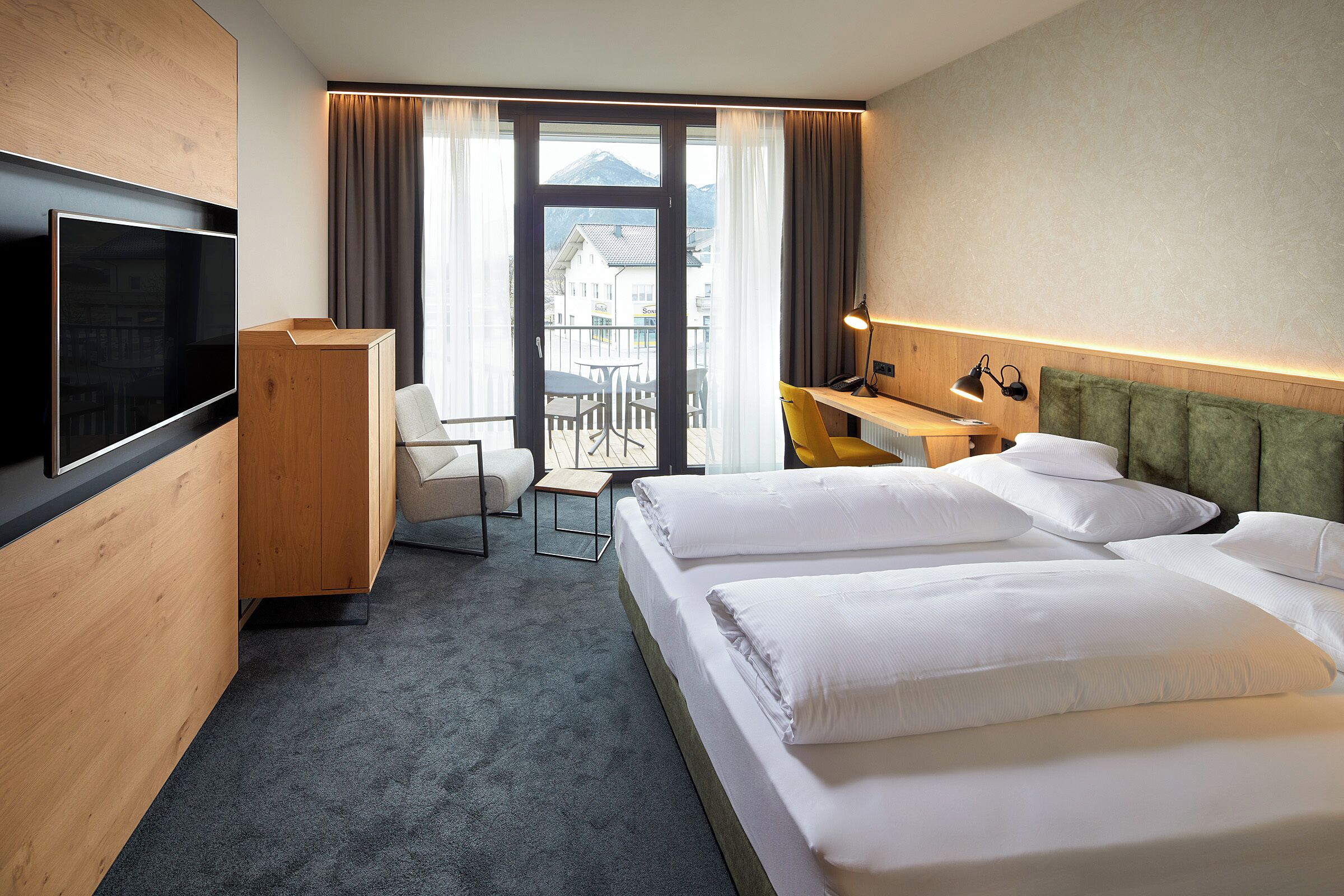 Une chambre d’hôtel avec un grand lit, un bureau, une chaise, une télévision et une vue sur les montagnes.