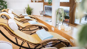 A spa room with multiple sun loungers, a small table with magazines, and potted plants. - Biohotel Leutascherhof (Leutasch)