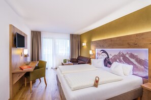 Habitación de hotel con cama, dos mesitas de noche, un escritorio con silla, televisor montado en la pared y decoración de pared con temática de montaña.