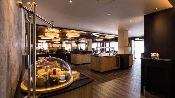 A modern hotel lobby with a central island featuring a glass dome display of food items, wooden flooring, and contemporary lighting fixtures. - Biohotel Leutascherhof (Leutasch)