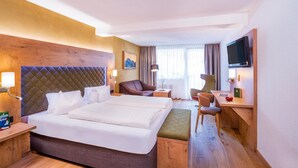 A hotel room with a large bed, a desk, a chair, a TV, and a window with curtains. - Biohotel Leutascherhof (Leutasch)