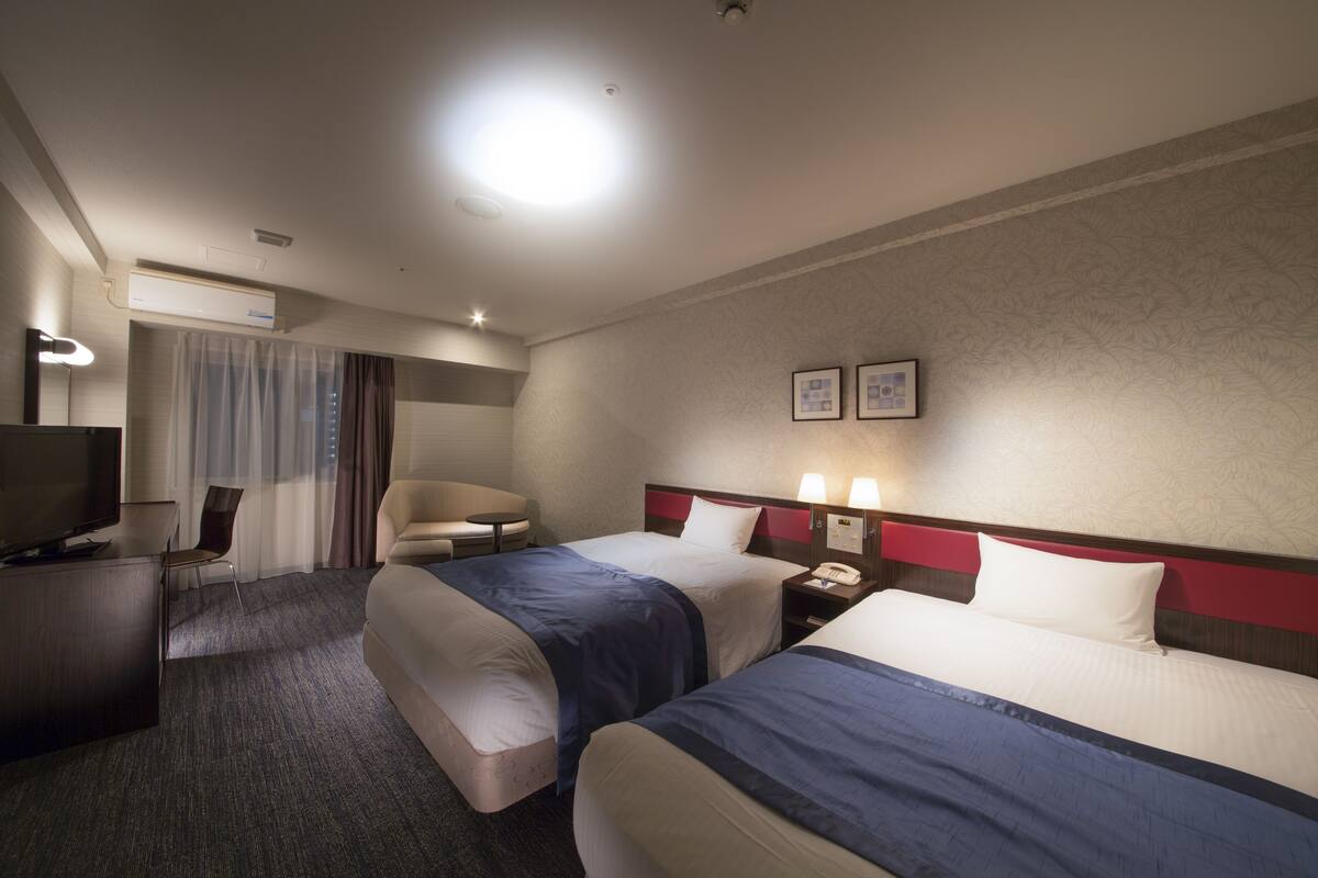 A hotel room with two beds, a desk with a TV, a chair, and a small table.