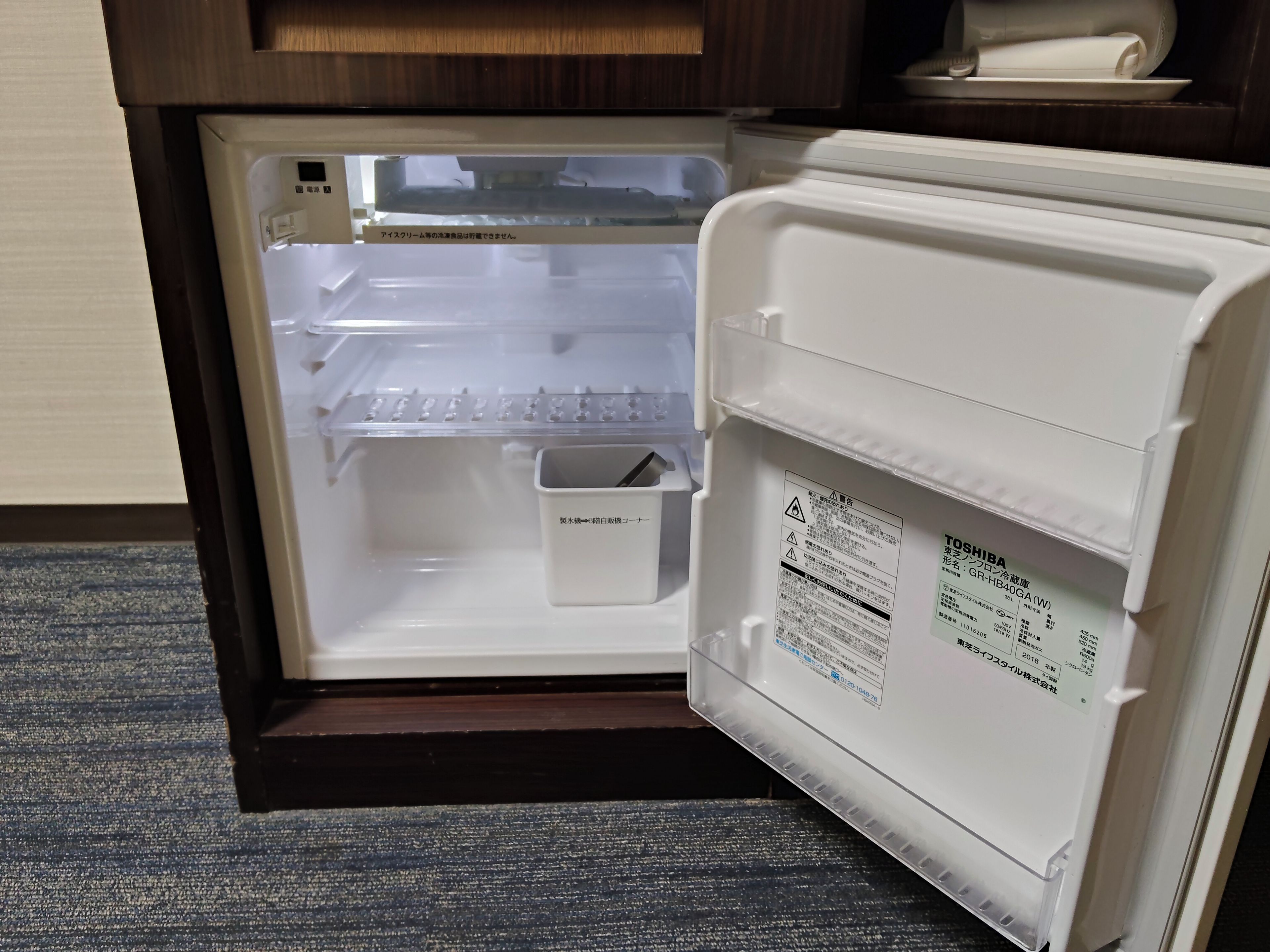 An open refrigerator with a water dispenser and a small storage bin inside.