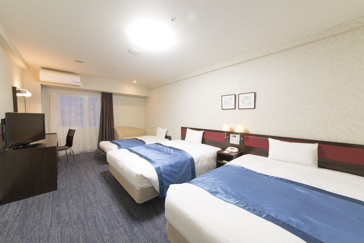 A hotel room with two beds, a desk, a TV, and a window with curtains.