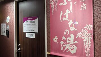 Habitació d'hotel amb una porta de fusta, una zona de recepció amb una quiosc digital i un distintiu rosa amb caràcters japonesos.