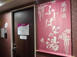 A hotel room with a wooden door, a reception area with a digital kiosk, and a pink banner with Japanese characters.