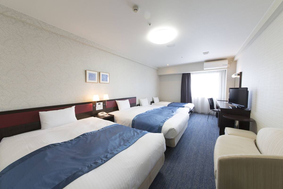 A hotel room with two beds, a desk, a chair, and a television.