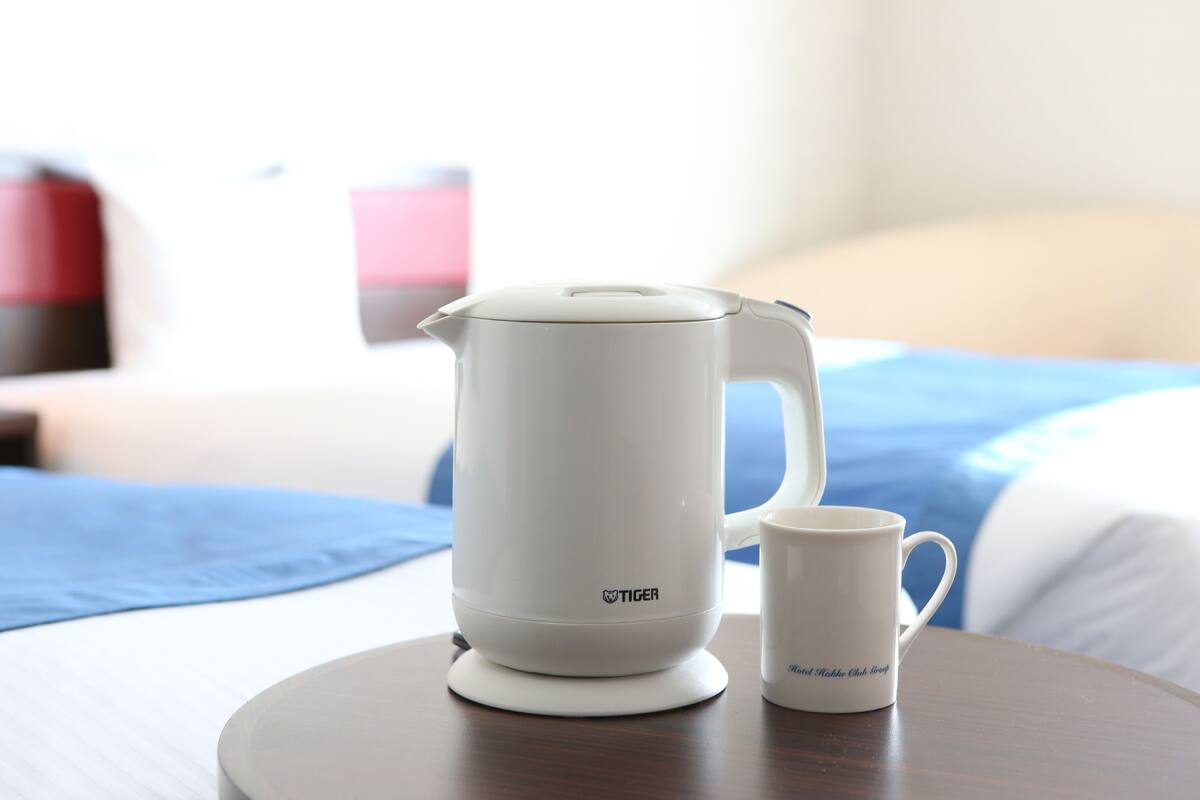 A white electric kettle and a mug on a round table in a hotel room.