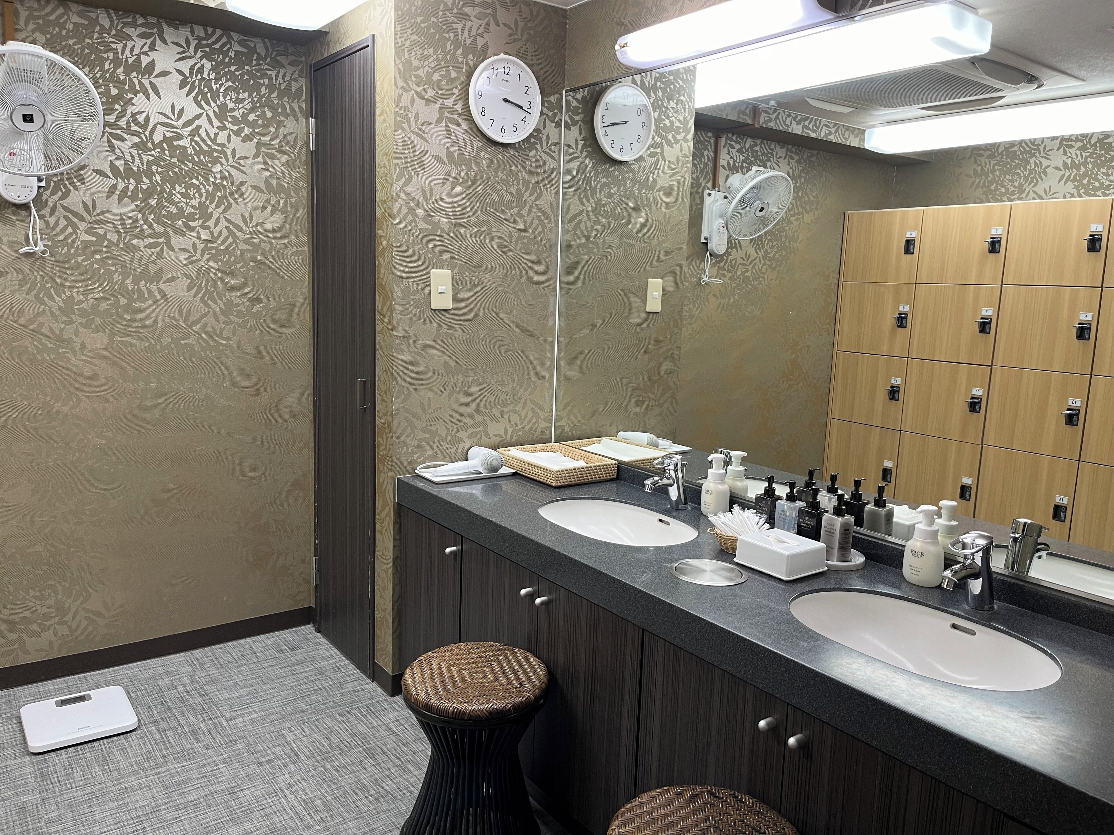 Un baño moderno con dos lavamanos, un espejo y un reloj en la pared.