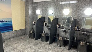 A public restroom with granite walls, multiple sinks, and mirrors. There are toiletries on the wall and a clock on the left. - Hotel Hokke Club Shonan - Fujisawa (Fujisawa)