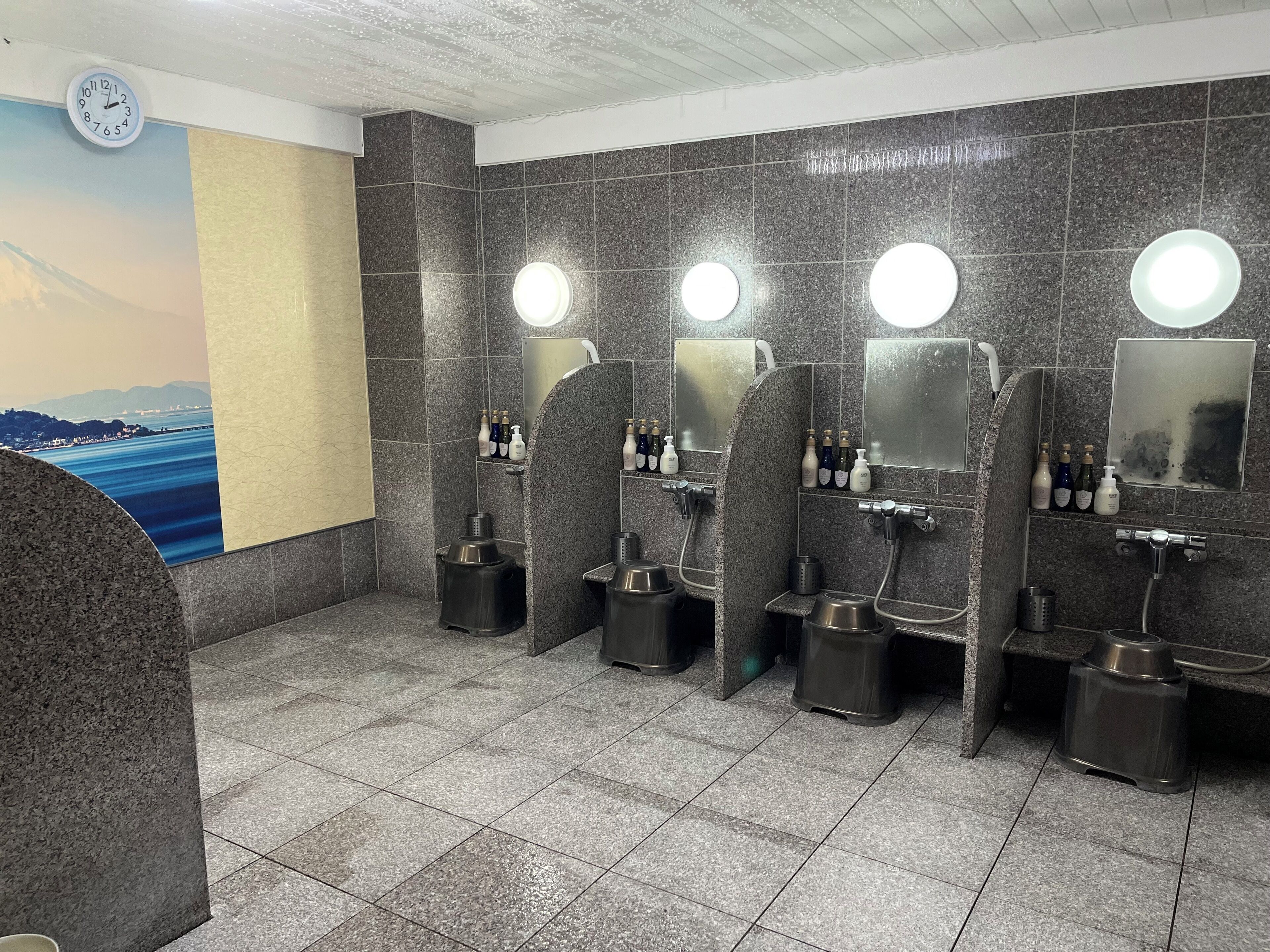 A public restroom with multiple stalls, each equipped with a mirror, soap dispenser, and a hand dryer.