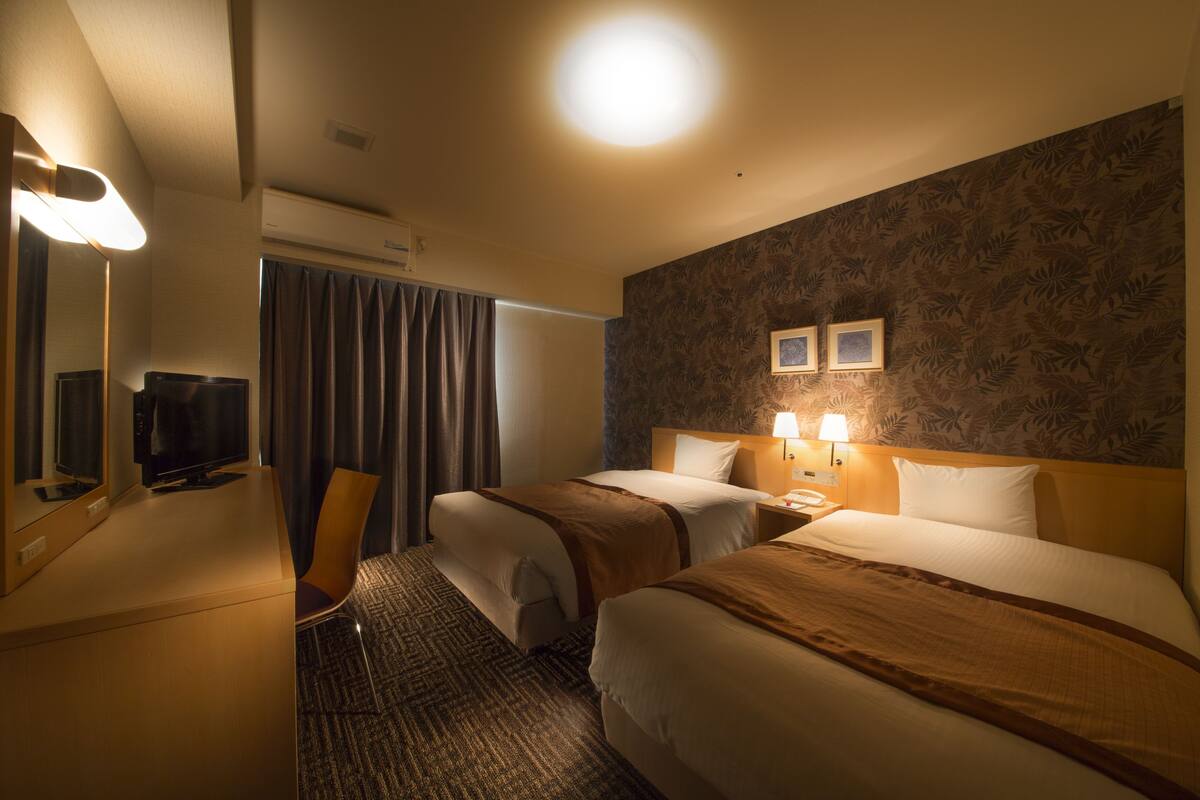 A hotel room with two beds, a desk, a chair, a television, and a window with curtains.