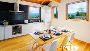 A modern kitchen with a wooden ceiling, a built-in stove, and a large window overlooking a scenic landscape. - Wagaya (Hakuba)