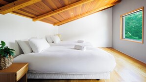 A modern bedroom with a large bed, wooden ceiling beams, a large window with a view of greenery, and a bedside table with a plant. - Wagaya (Hakuba)