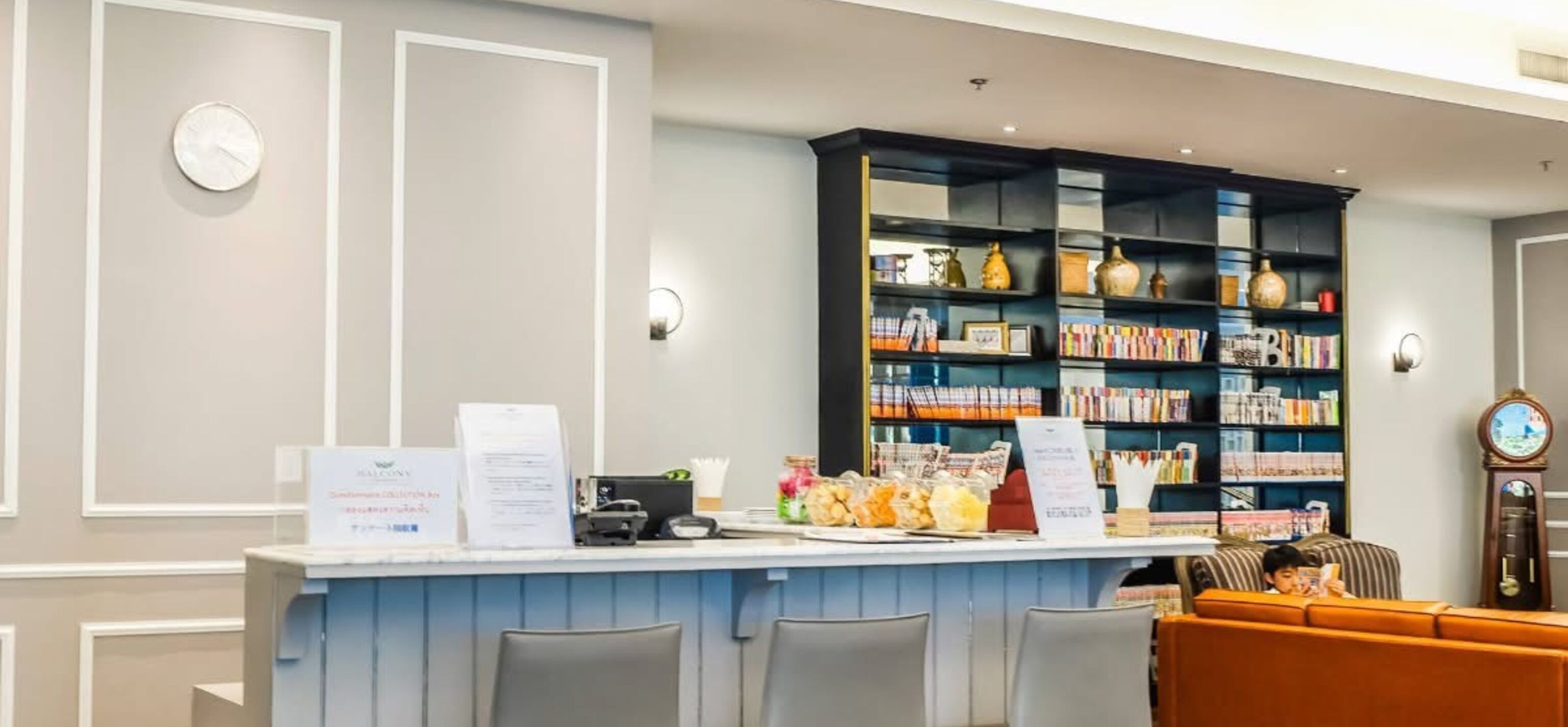 Un área de recepción con mostrador, asientos y una estantería llena de libros y objetos decorativos.