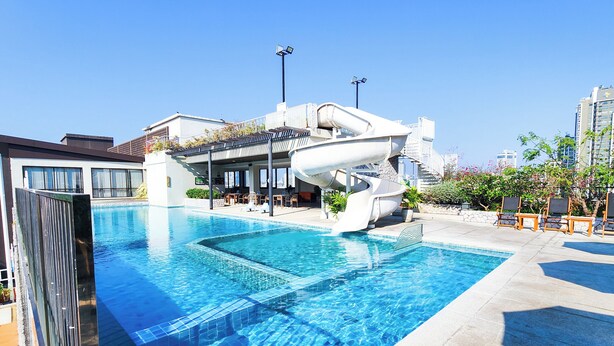 Ein Schwimmbad mit Wasserrutsche, Liegestühlen und einem Gebäude mit großen Fenstern.