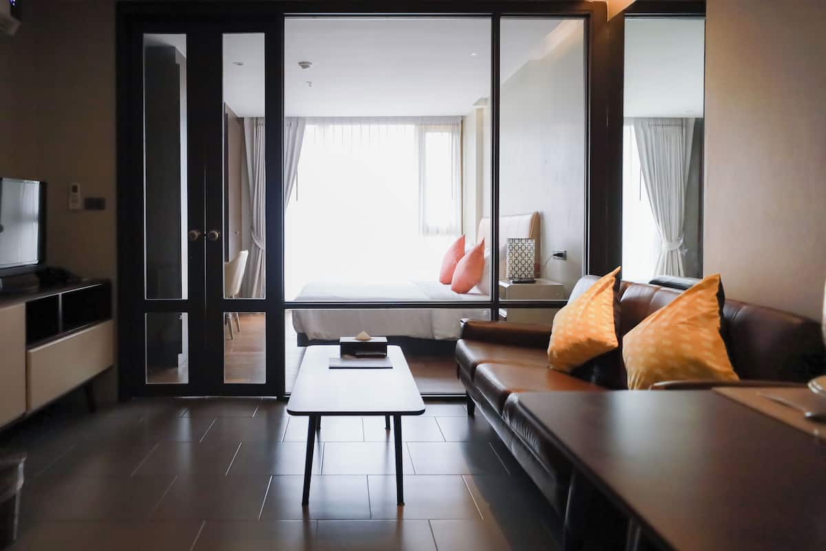 Ein modernes Hotelzimmer mit einer Couch, einem kleinen Tisch, einem Fernseher und einer Glastür, die auf einen Balkon führt.