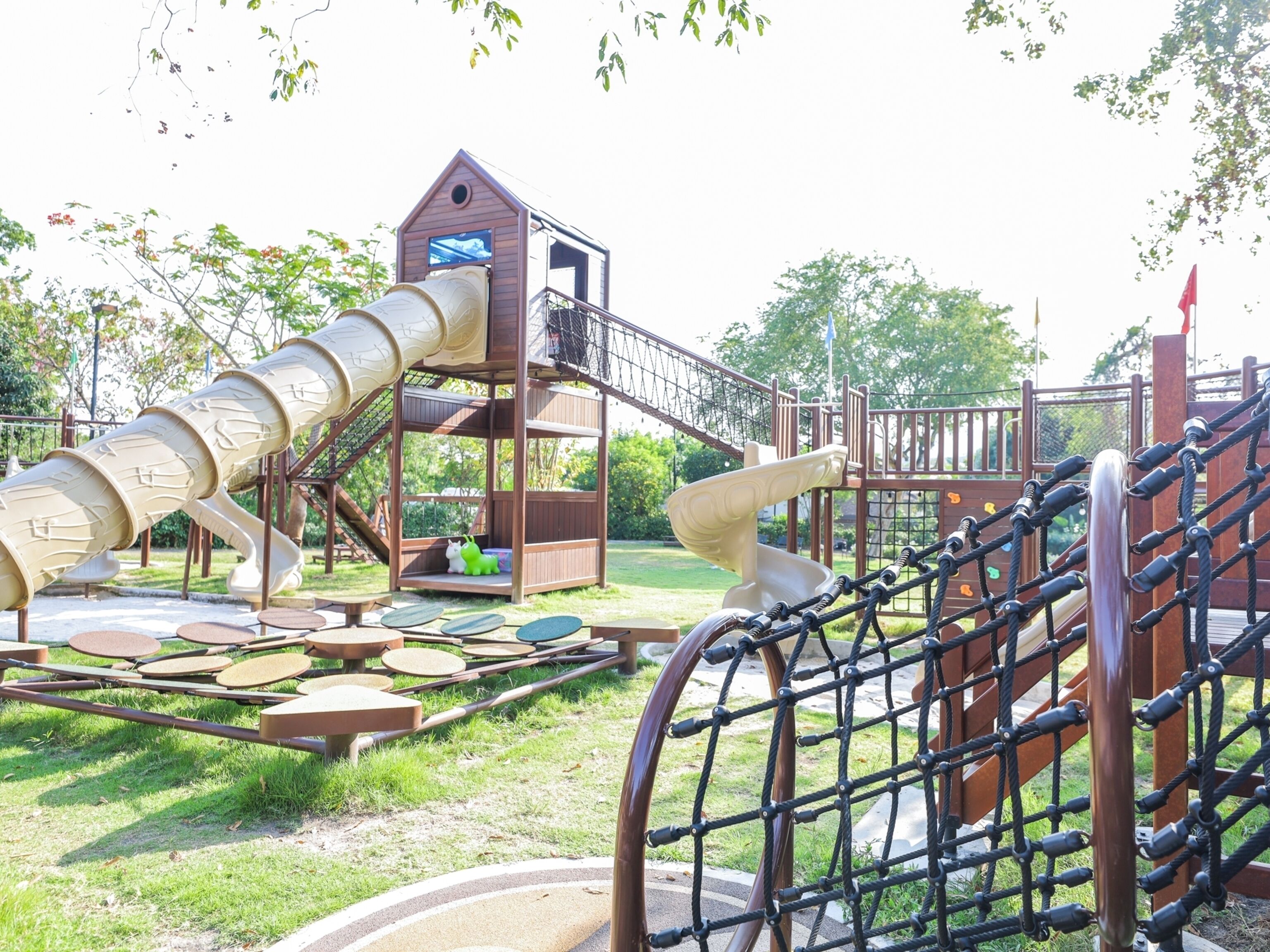 Un parque infantil con tobogán, red de escalada y una casita.