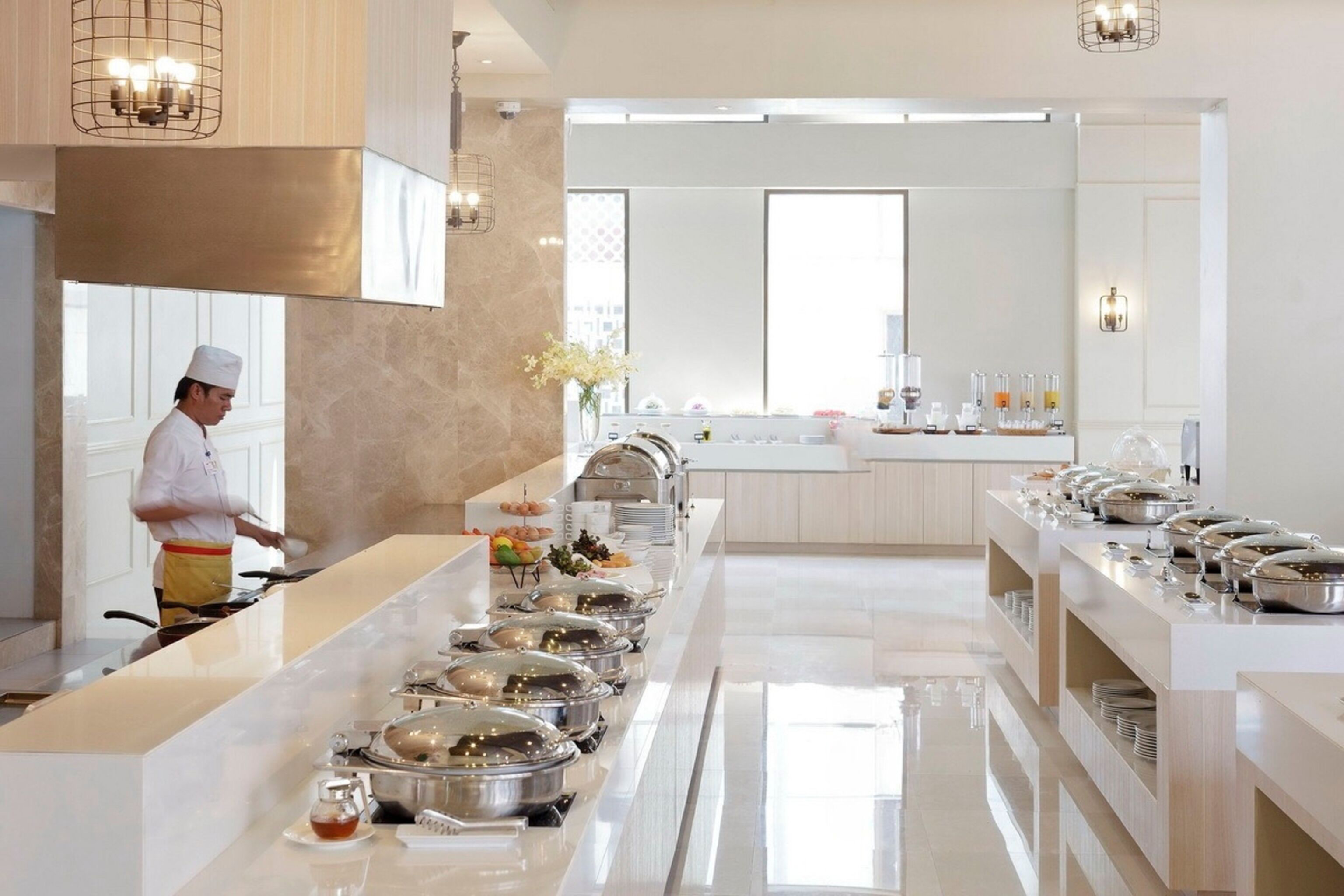 Una cocina moderna de hotel con barra libre, un chef preparando alimentos y un ambiente limpio y bien iluminado.