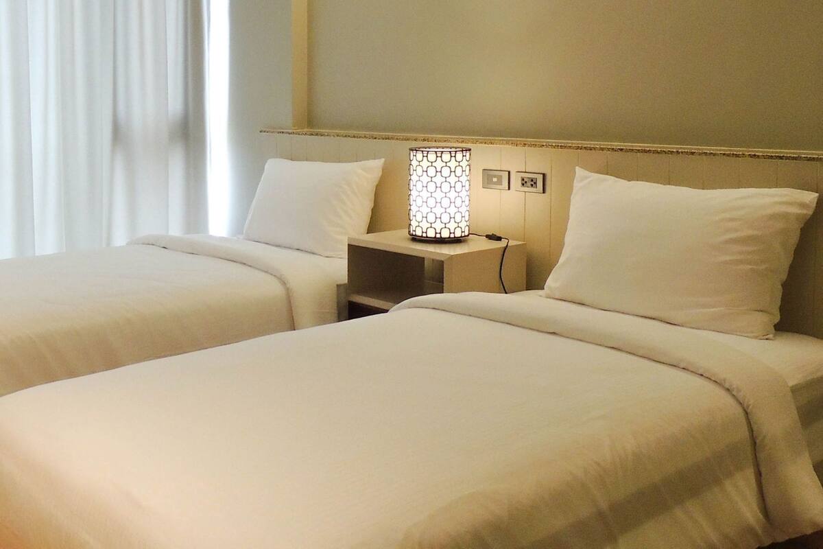 Ein Hotelzimmer mit zwei Betten, einem Nachttisch mit Lampe und einem Fenster mit Vorhängen.