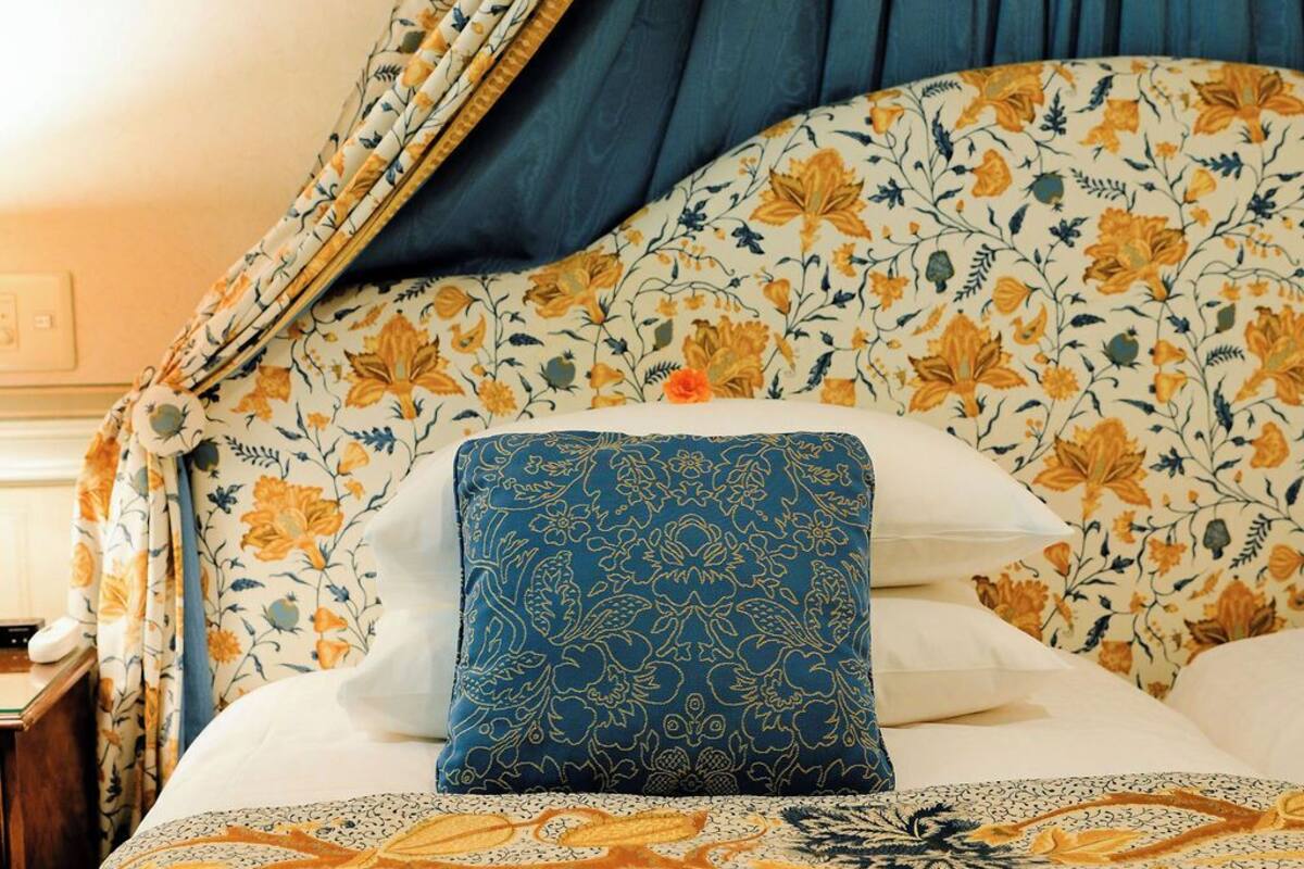 Un lit avec une couvre-lit à motifs floraux, un oreiller bleu et un livre posé sur le lit.