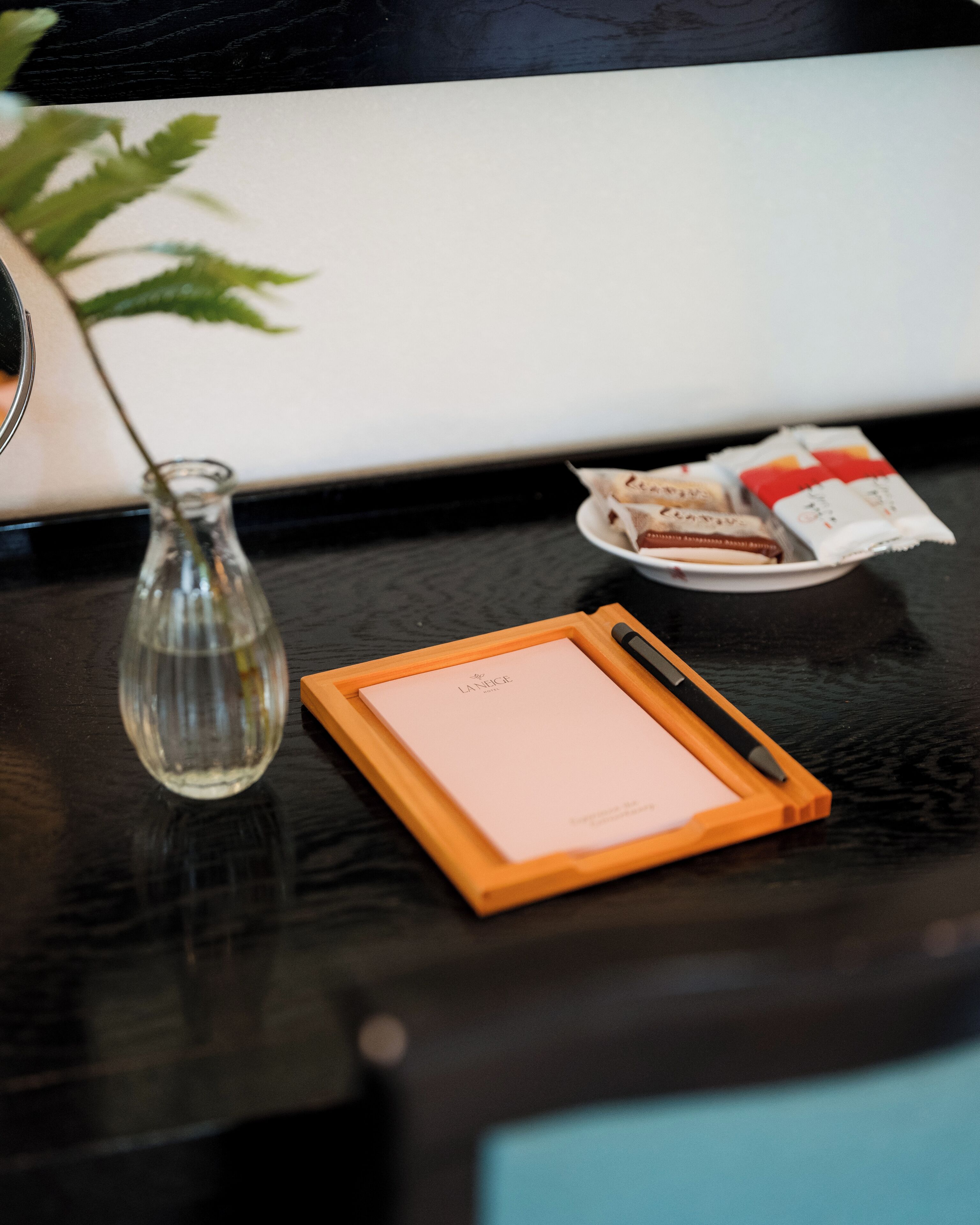 A desk with a notepad, pen, a small vase, and a plate with snacks.