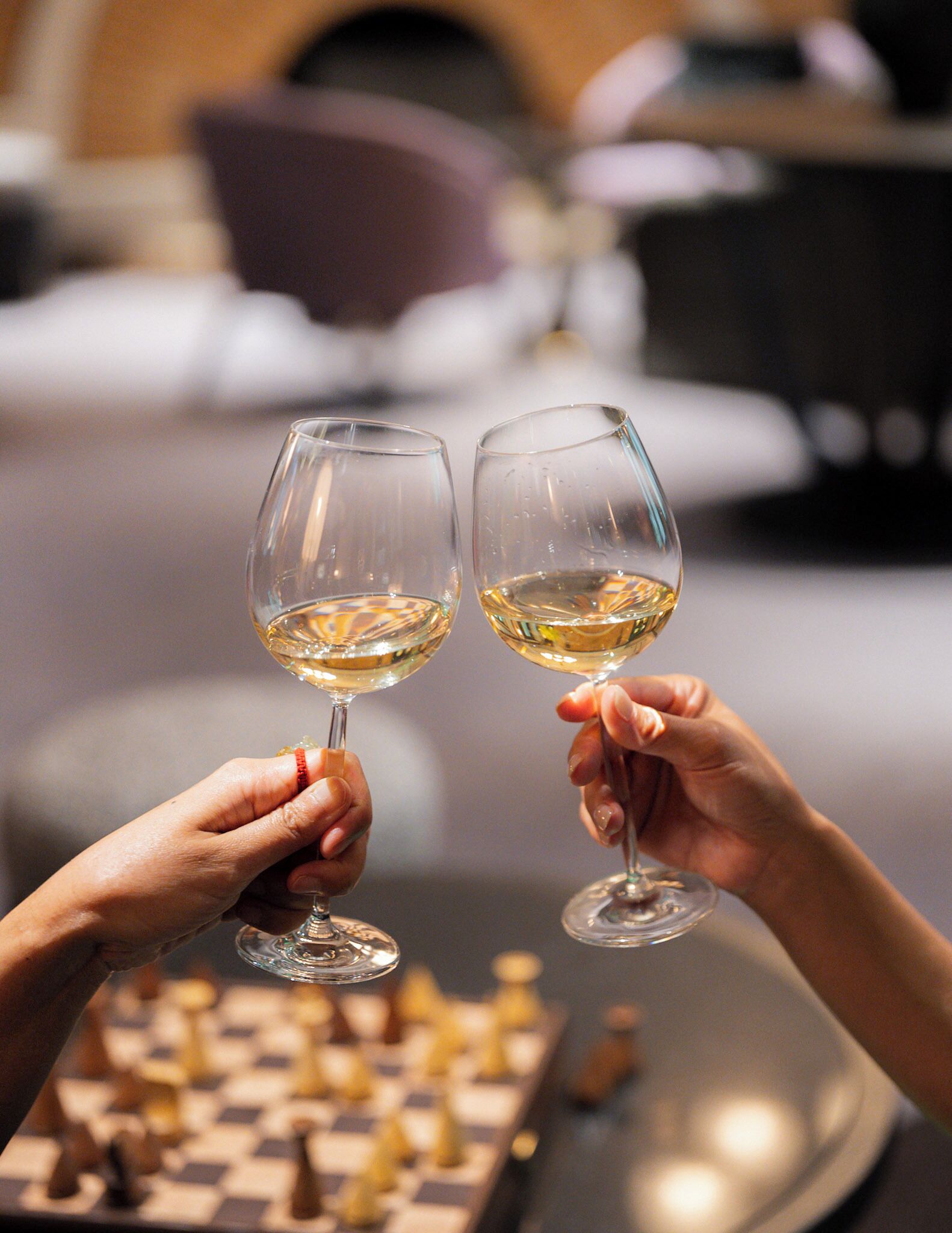 Two people holding wine glasses with a chessboard in the foreground.