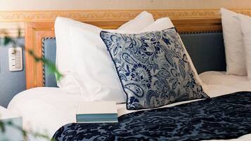Un lit bien fait, agrémenté d’oreillers blancs et bleus à motifs, d’une couvre-lit bleu foncé et de deux tableaux floraux encadrés accrochés au mur.