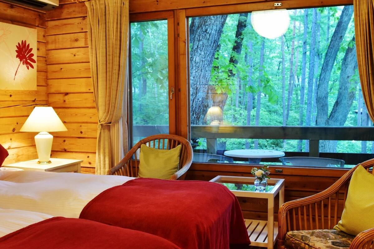 Une chambre confortable dans un chalet, avec deux lits, une petite table, des chaises en osier et une grande fenêtre donnant sur la forêt.
