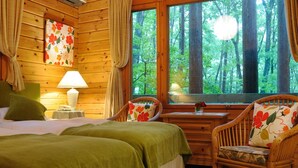 Een gezellig houten kamer met een bed, twee stoelen, een klein tafeltje en een raam met uitzicht op een bos.
