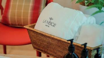 Uma cesta de vime com uma toalha branca identificada com 'LA NEIGE HOTEL' e uma cadeira vermelha com almofada xadrez.