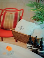 Uma cesta de vime com uma toalha branca identificada com 'LA NEIGE HOTEL' e uma cadeira vermelha com almofada xadrez.