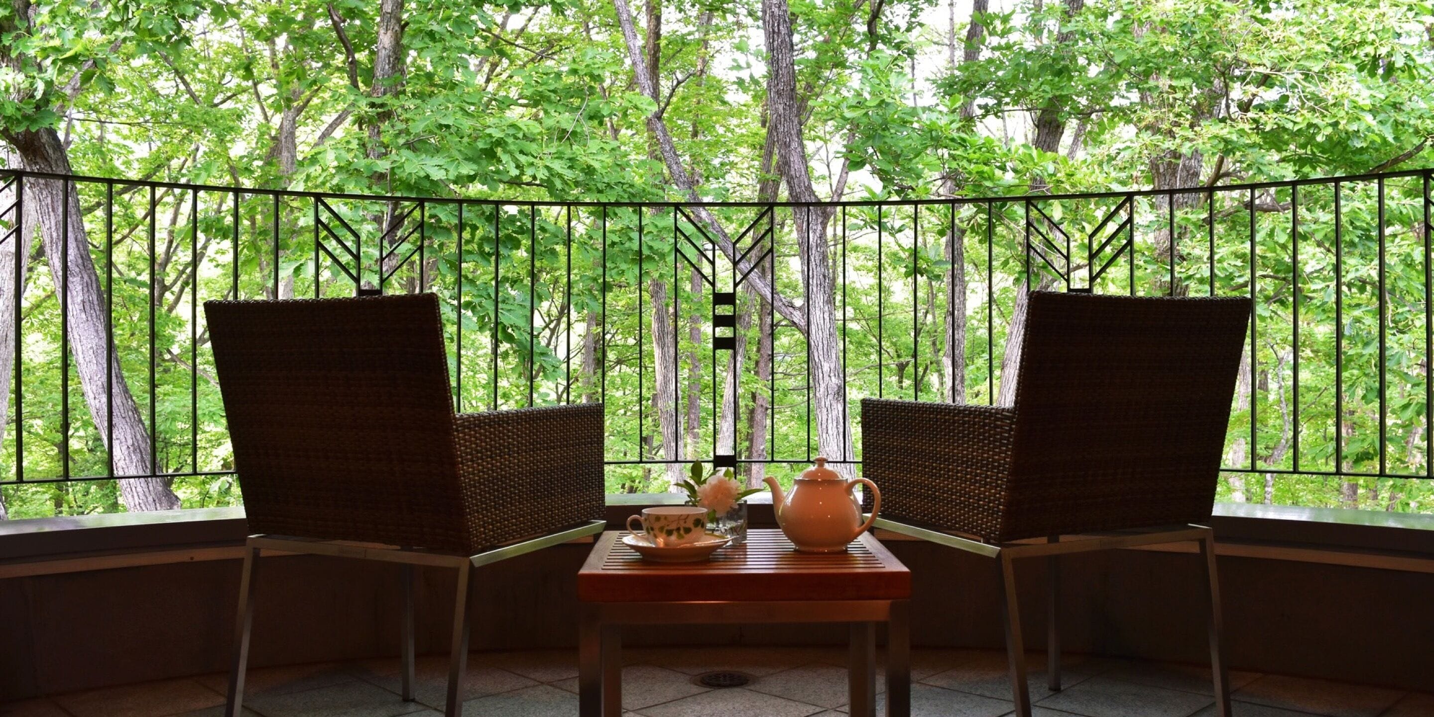 Una habitación con dos sillones de mimbre orientados hacia una ventana con vistas a un bosque. En el centro, una mesa con una tetera y una taza.