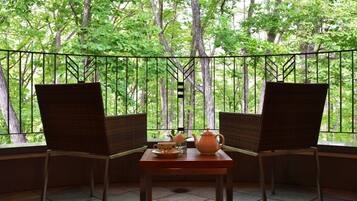 Una habitación con dos sillones de mimbre orientados hacia una ventana con vistas a un bosque. En el centro, una mesa con una tetera y una taza.