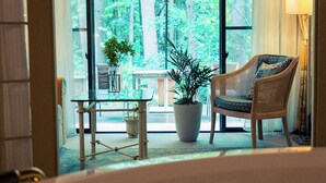 Een hotelkamer met een groot raam, een rieten stoel, een tafeltje en een kamerplant.