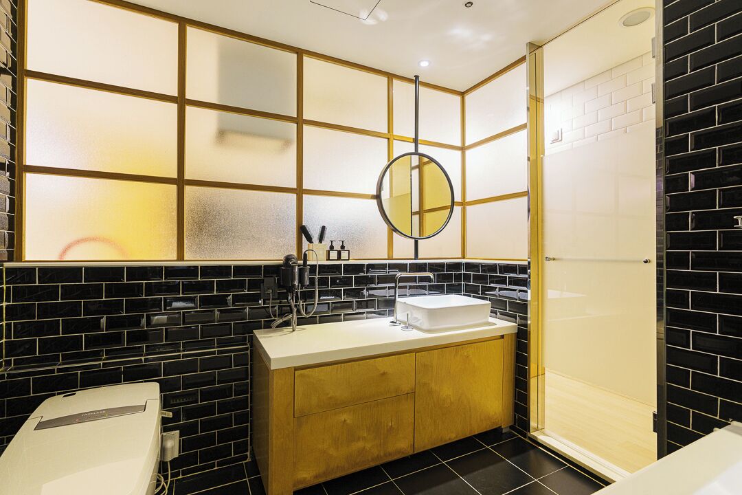 Um banheiro moderno com painel de azulejos preto e branco, um móvel de madeira com cuba branca, um espelho redondo e box de vidro para o chuveiro.