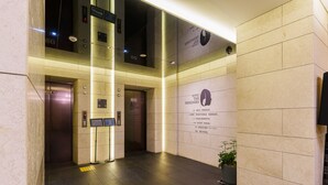 A hotel lobby with a modern design, featuring a central column, elevators, and a sign listing amenities like a lobby, front lounge, and guest room.