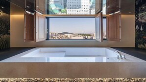 A modern bathroom with a large bathtub and a view of a cityscape through an open window.
