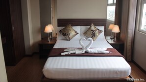 A hotel room with a large bed, two nightstands with lamps, a wooden wardrobe, and a view through the window. - Shaw Residenza Suites (Mandaluyong)