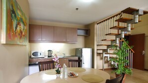 A dining area with a round table, chairs, a microwave, a refrigerator, and a staircase with a railing. - Shaw Residenza Suites (Mandaluyong)