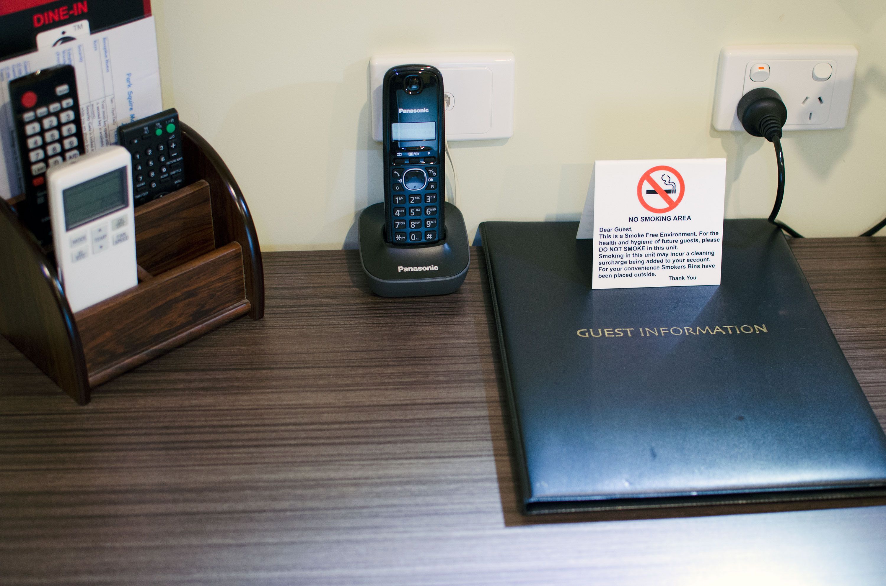 A hotel desk with a Panasonic phone, a "No Smoking Area" sign, and a "Guest Information" booklet.