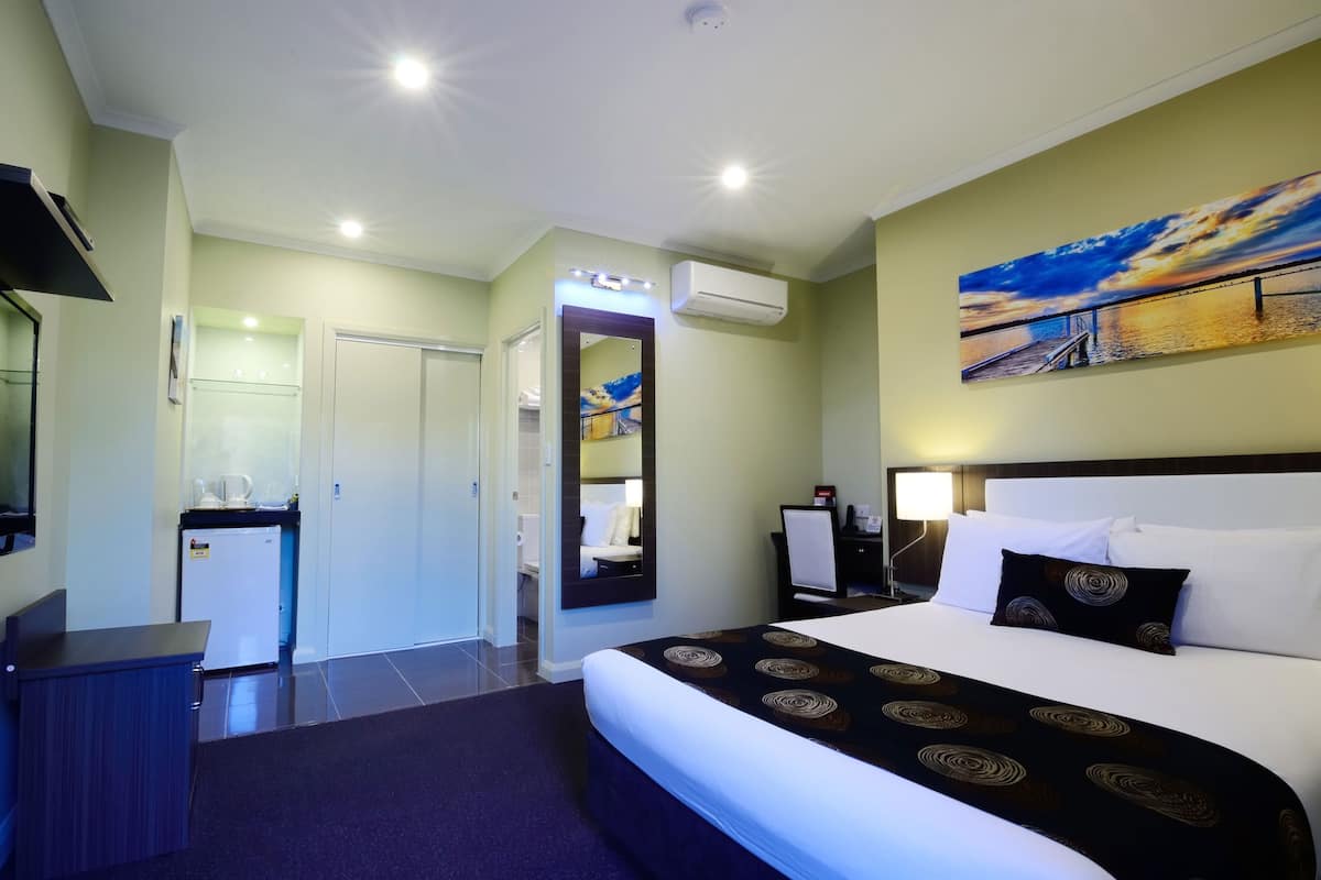 Una habitación de hotel con una cama grande, un escritorio, una pequeña cocina y un baño.