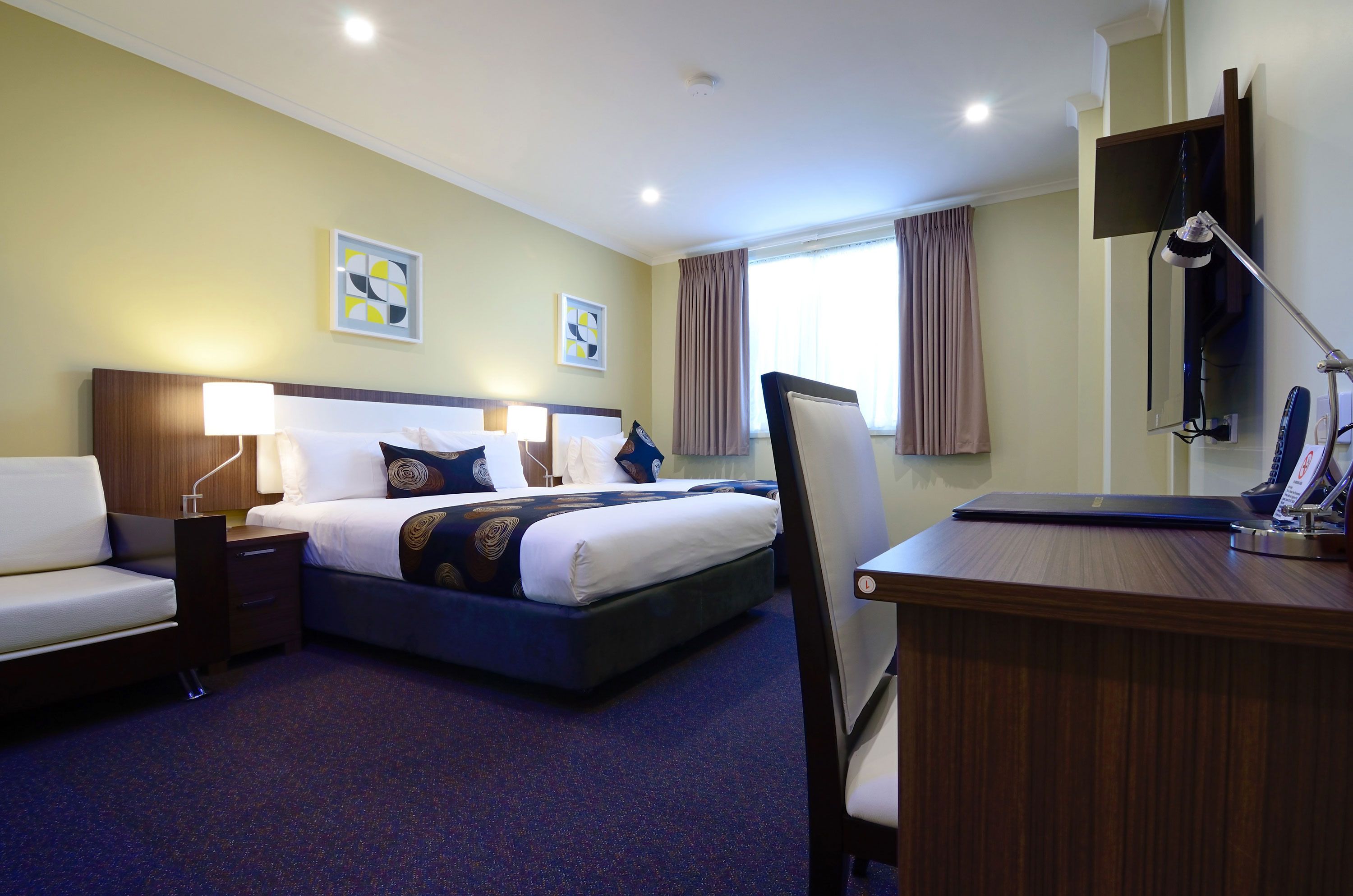 Una habitación de hotel con cama, mesitas de noche, escritorio, silla y televisión.