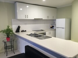 Uma cozinha moderna com armários brancos, uma pia de aço inoxidável, um micro-ondas e uma geladeira.