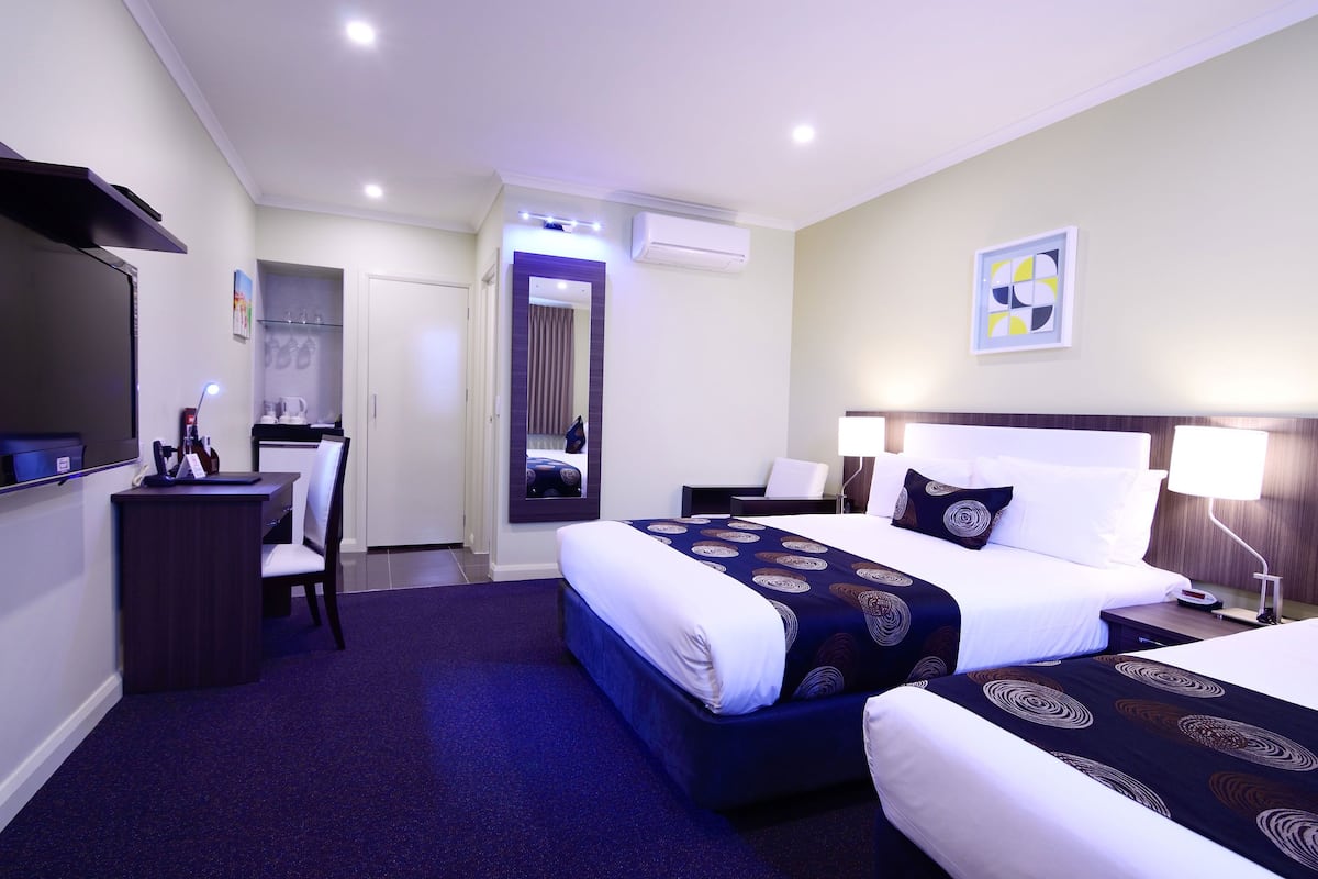 Habitación de hotel con dos camas, un escritorio, una silla y un televisor.