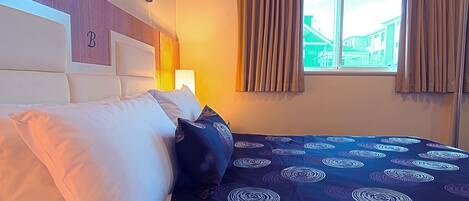 A hotel room with a bed, a headboard with a letter 'B', and a window with curtains.