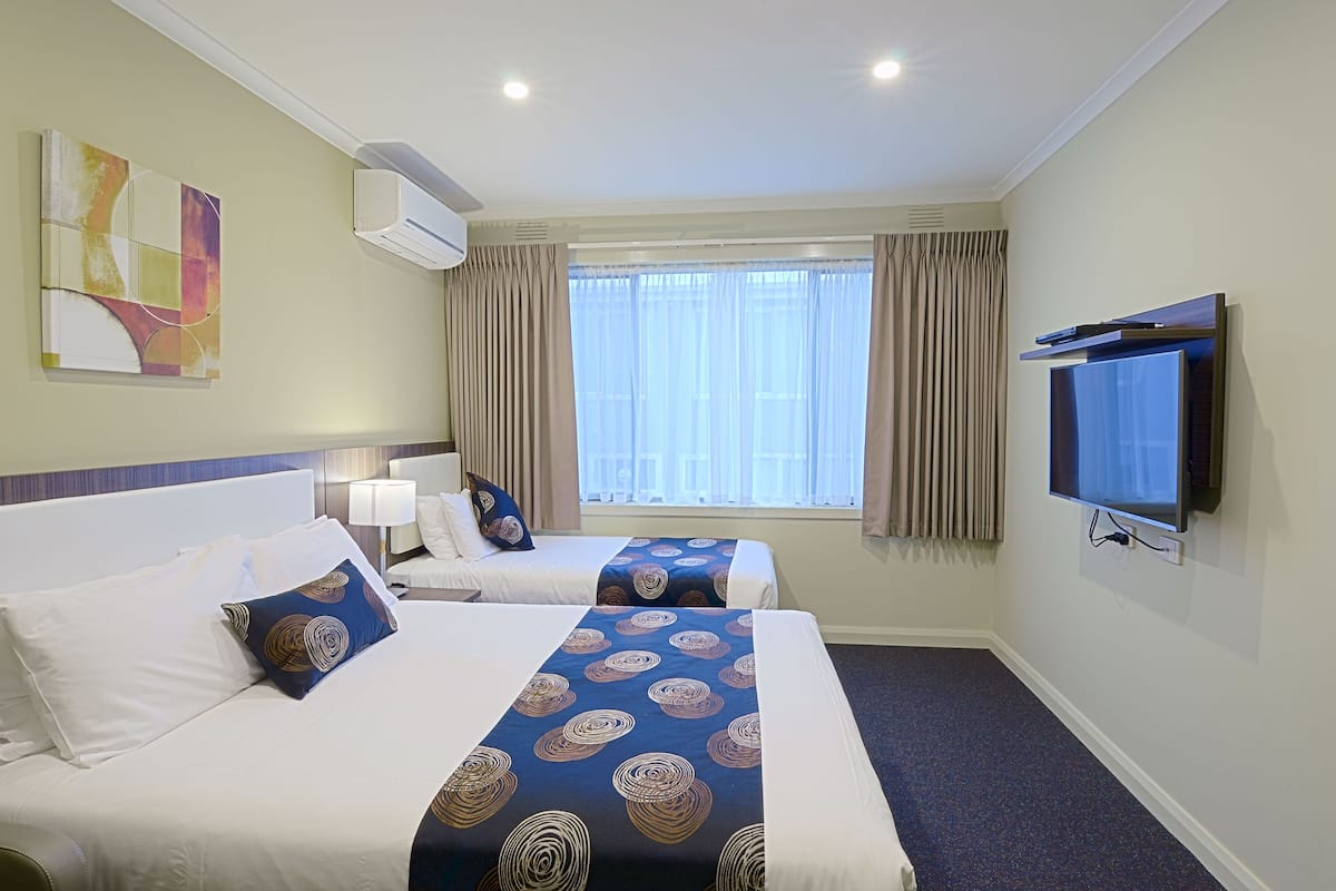 Habitación de hotel con dos camas, televisión, aire acondicionado y ventana con cortinas.